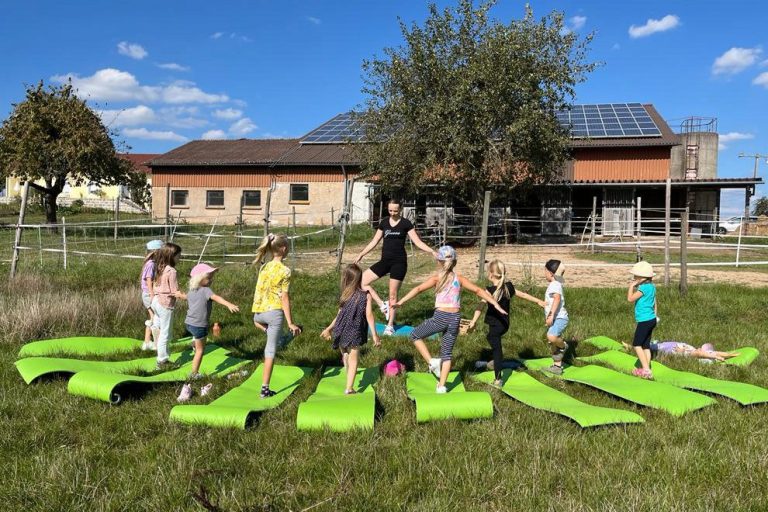 Kinderyoga - Yoga-Spaß für die Kleinen Mehrere Kinder machen gemeinsam Yoga-Übungen draußen auf einer Wiese bei klarem Himmel.