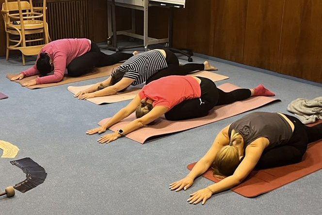 Firmen-Kurse - Team-Yoga für Unternehmen Mehrere Mitarbeitende eines Unternehmens machen gemeinsame Yoga-Übungen in einer Trainingshalle.