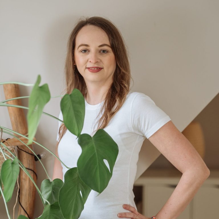 Professionelle Yoga-Trainerin - Über mich Yoga-Trainerin posiert neben Pflanze.
